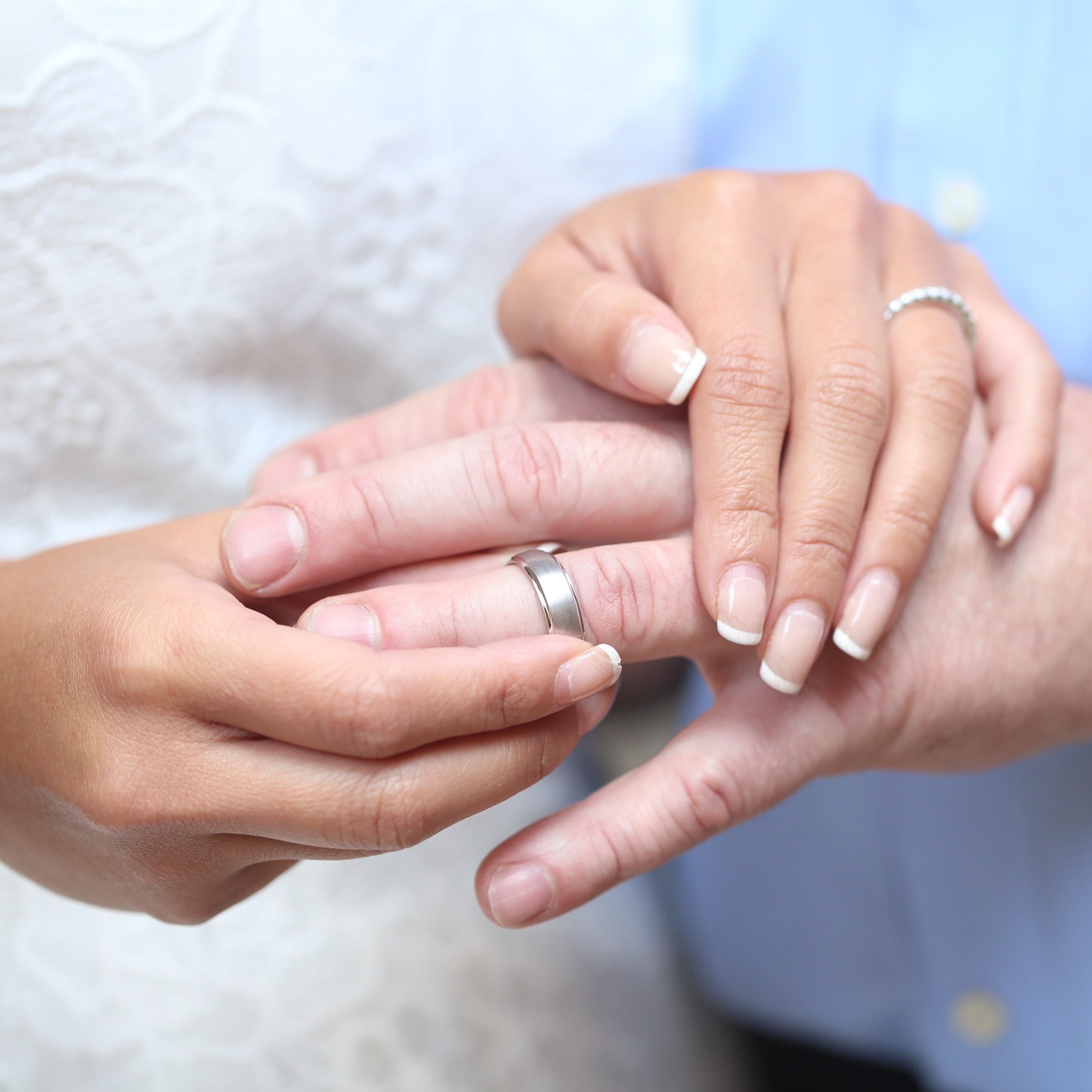 A woman putting on a white gold wedding band on her mans hand.