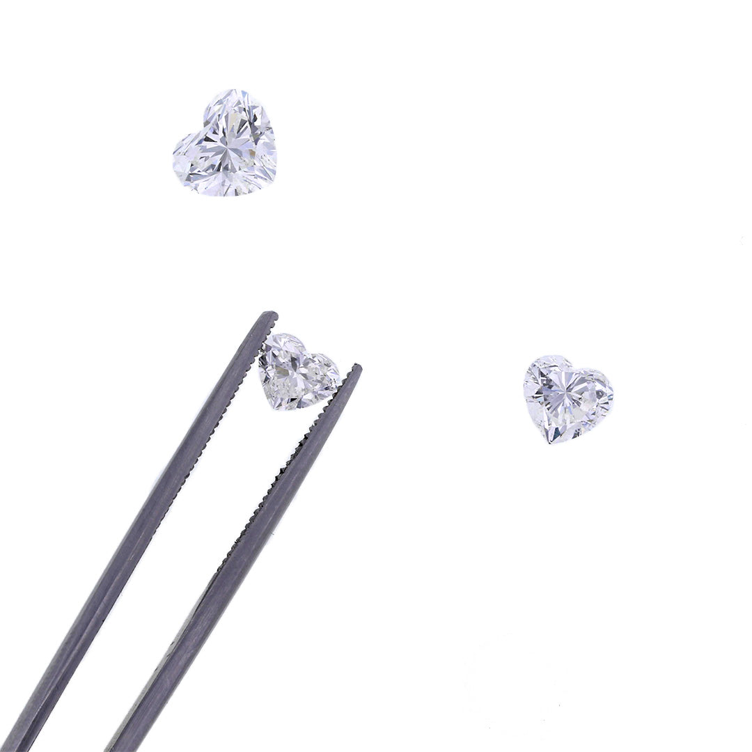 A tweezer holding a heart shaped diamond with two other ones next to it.