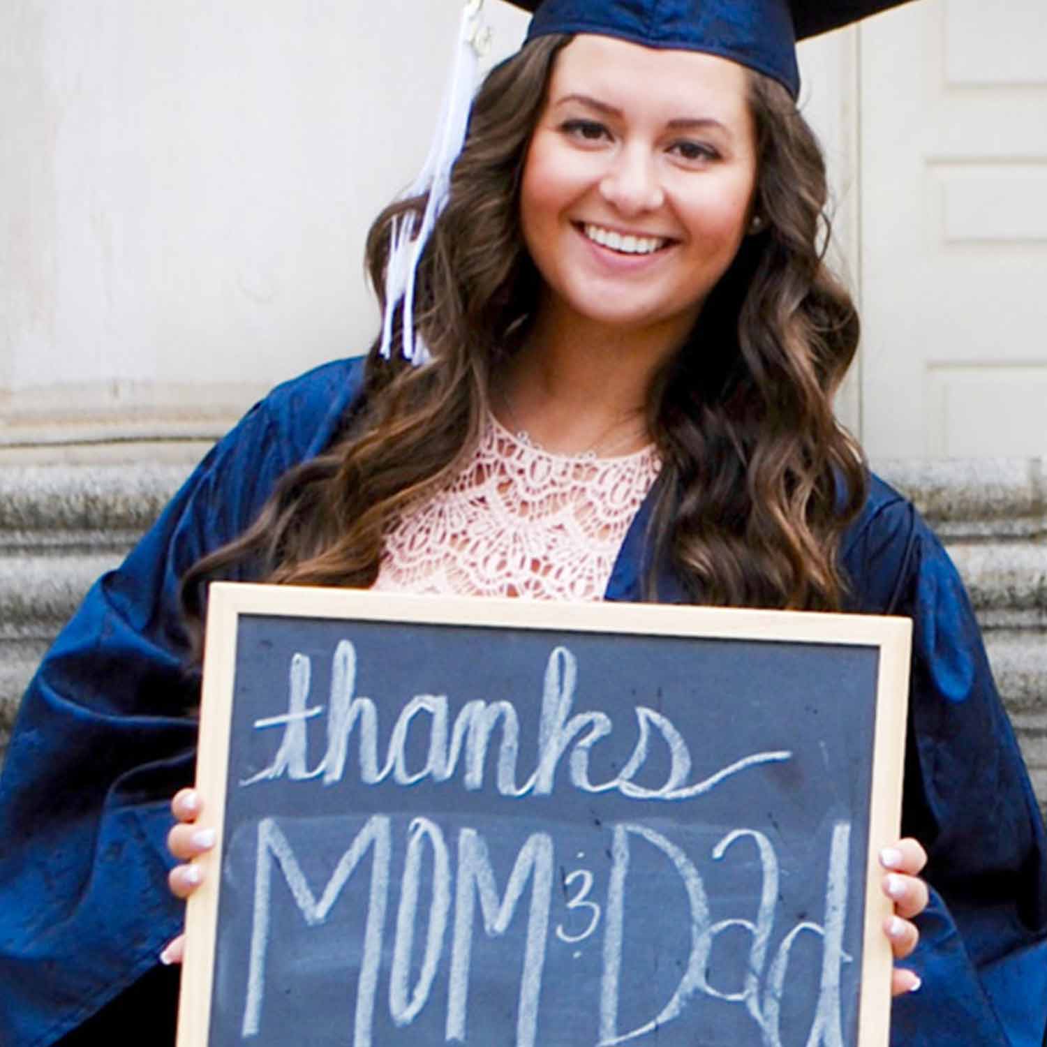 A  female graduate holding up a sign thanking her mom and dad.