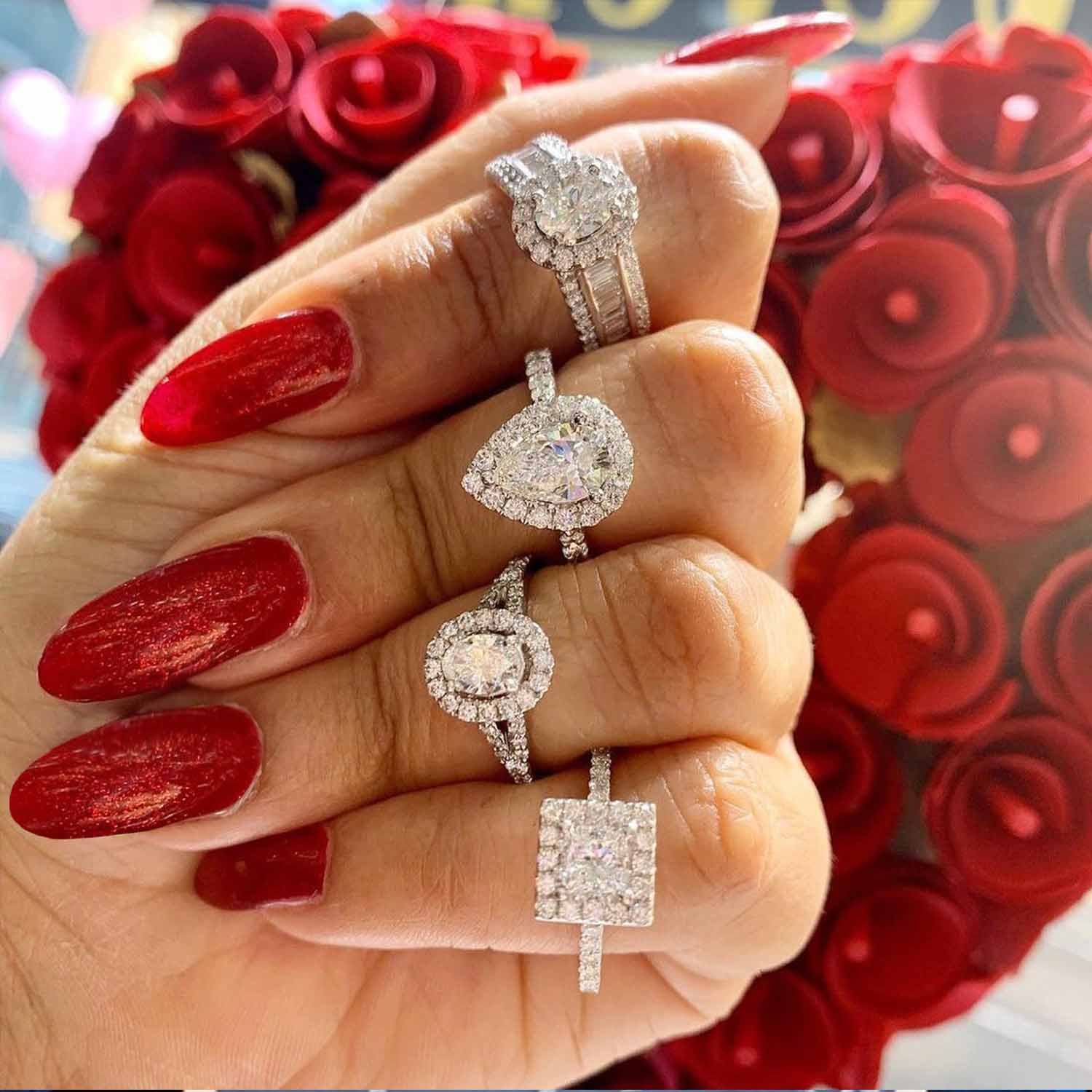 This image shows a woman's hand in front of a heart shaped rose bouquet with 4 different halo rings on her fingers.