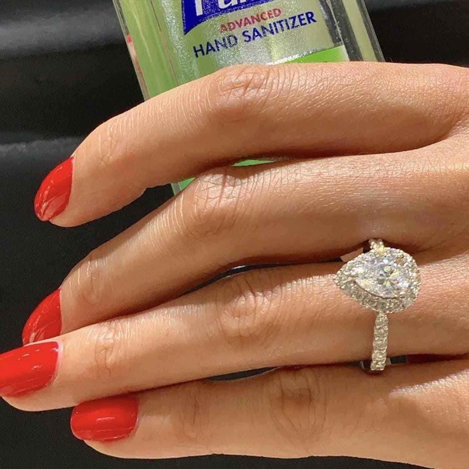 A woman holding hand sanitizer with one of our beautiful pear shaped engagement rings on.