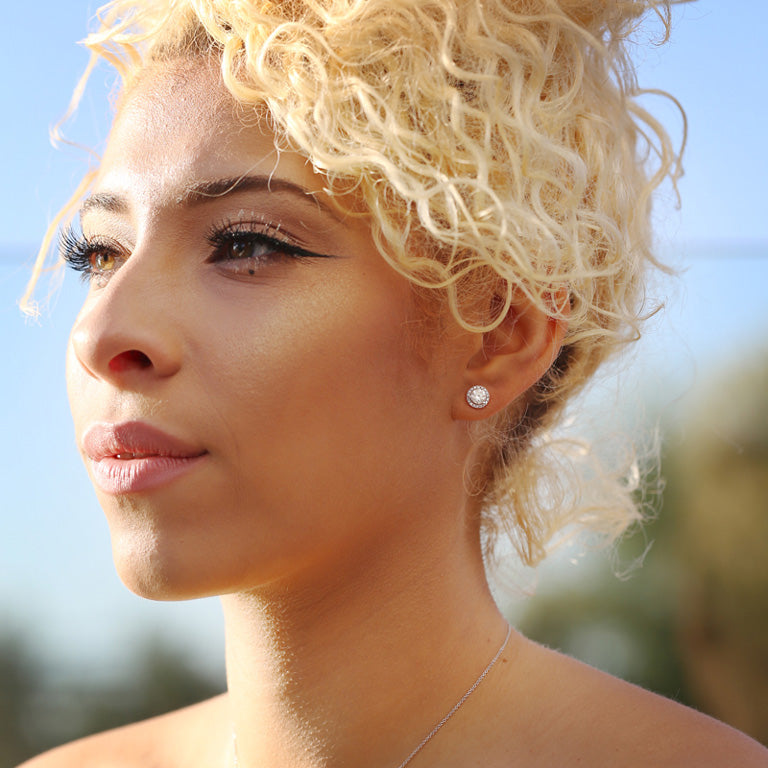 A blonde girl showing off earring jackets that give the studs a halo look.