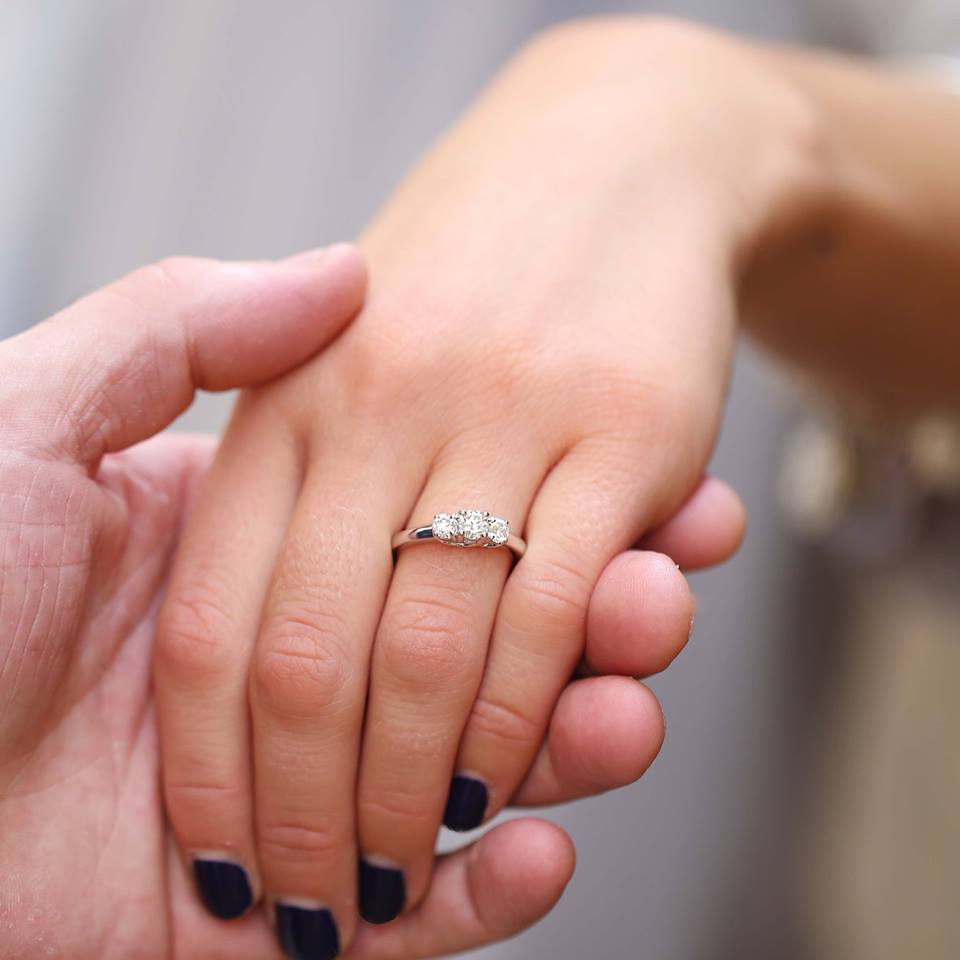 A man holding a woman's left hand showing off the diamond ring on her ring finger.
