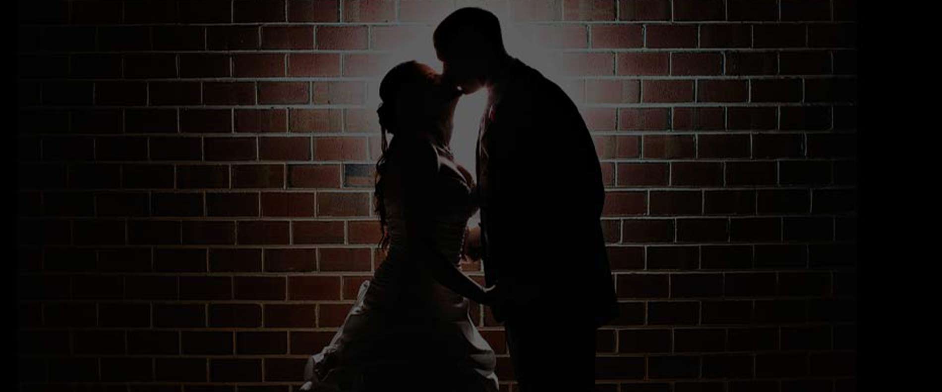 A bride and groom kissing in a brick backround.