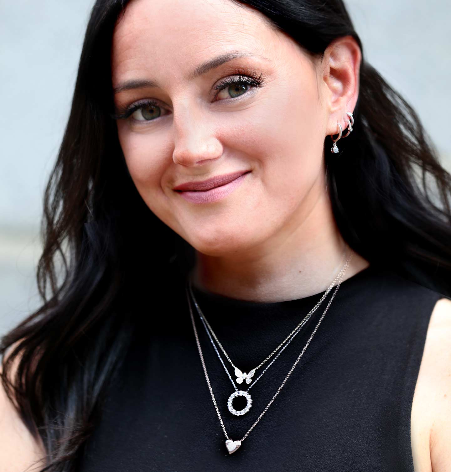 A woman wearing a butterfly, circle, and heart pendant and a cascade of hoop earrings. 