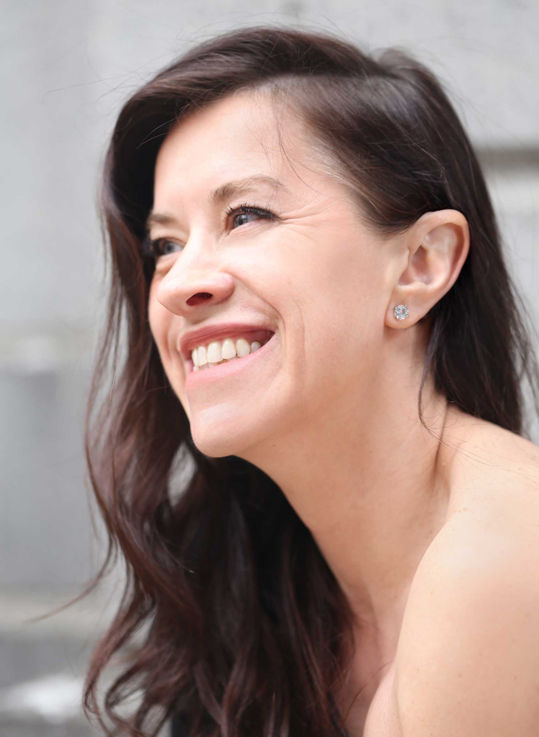 A brunette woman smiling wearing our Moonlight Aquamarine Stud Earrings.