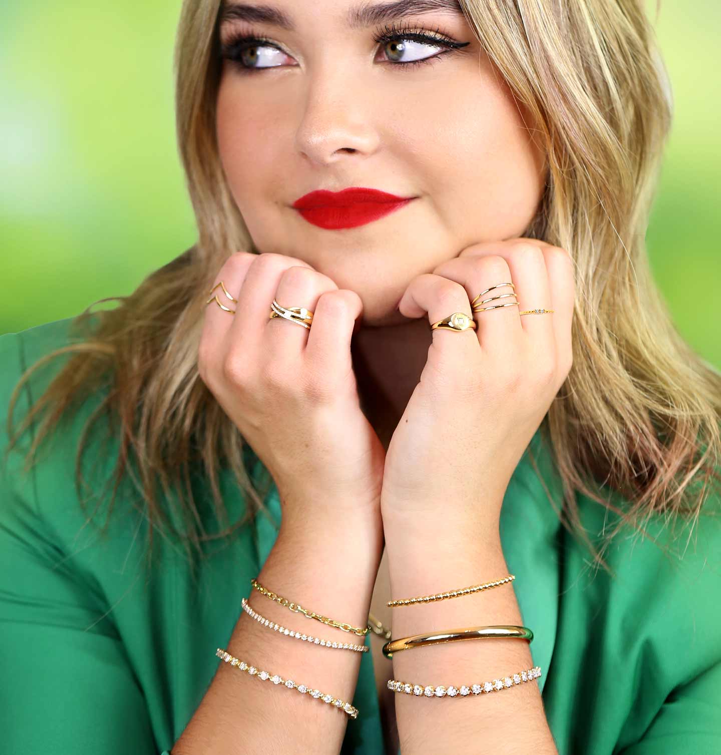 A women in green wearing stacked bracelets and rings made out of diamonds and 14 karat gold.