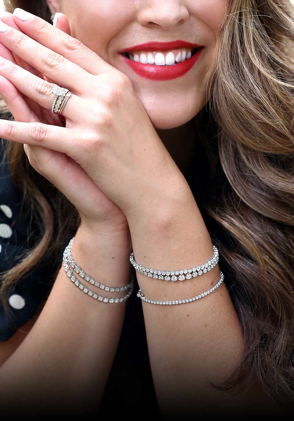 This image features a woman that has her hands together with our diamond bracelets on both arms. The bracelets we offer are tennis bracelets, bangle bracelets, and halo diamond bracelets along with different metal options like 14k yellow gold, white gold, and rose gold. 
