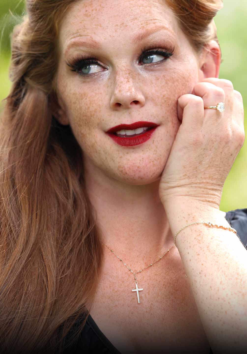 A women modeling a cross necklace and oval engagement ring.