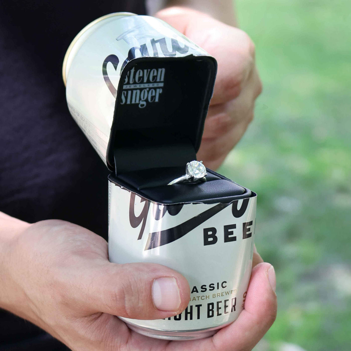 A Steven Singer Black Box with an engagement ring inside a cut open Garage Beer Can.
