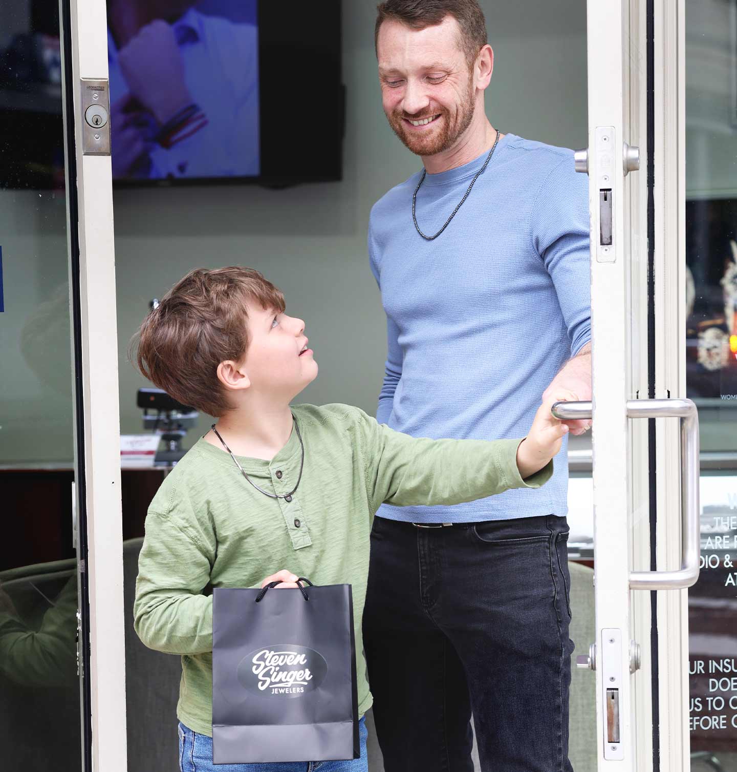 Man and his son standing in front of Steven Singer Jewelers store entrance, with the child holding a black gift bag.