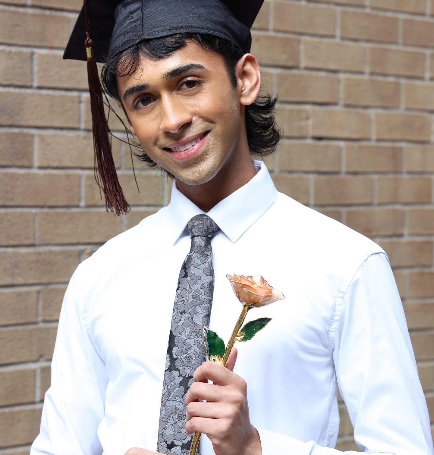 Graduate holding a real gold dipped rose in front of a brick wall.