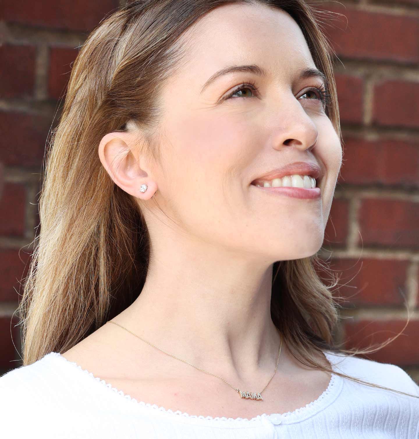 Woman wearing a necklace and classic diamond studs with a brick wall background.