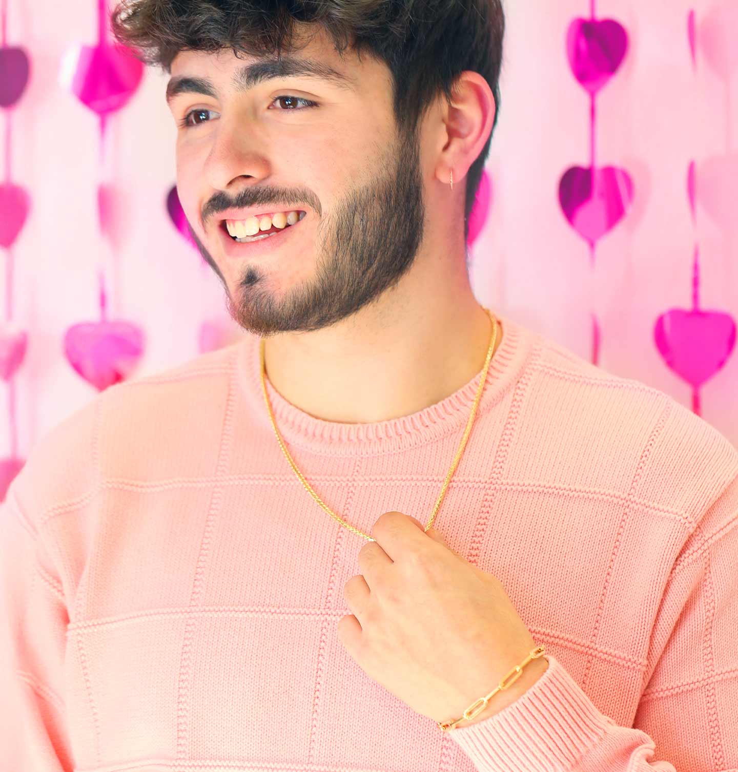 A man in a sweater wearing a gold necklace and bracelet.