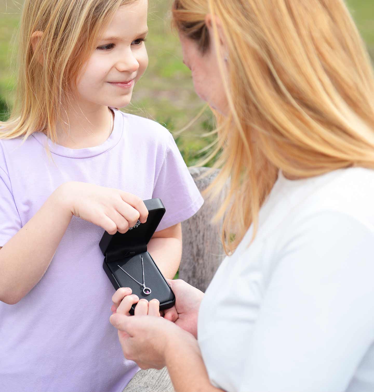 Woman and he daughter looking at a diamond necklace together outdoors.