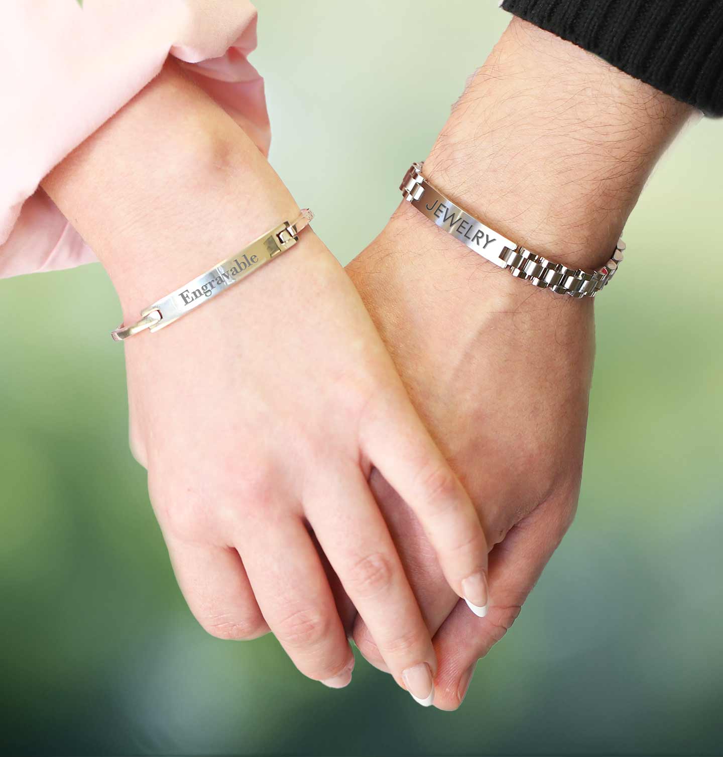 Two hands holding each other wearing silver bracelets with engraved text.