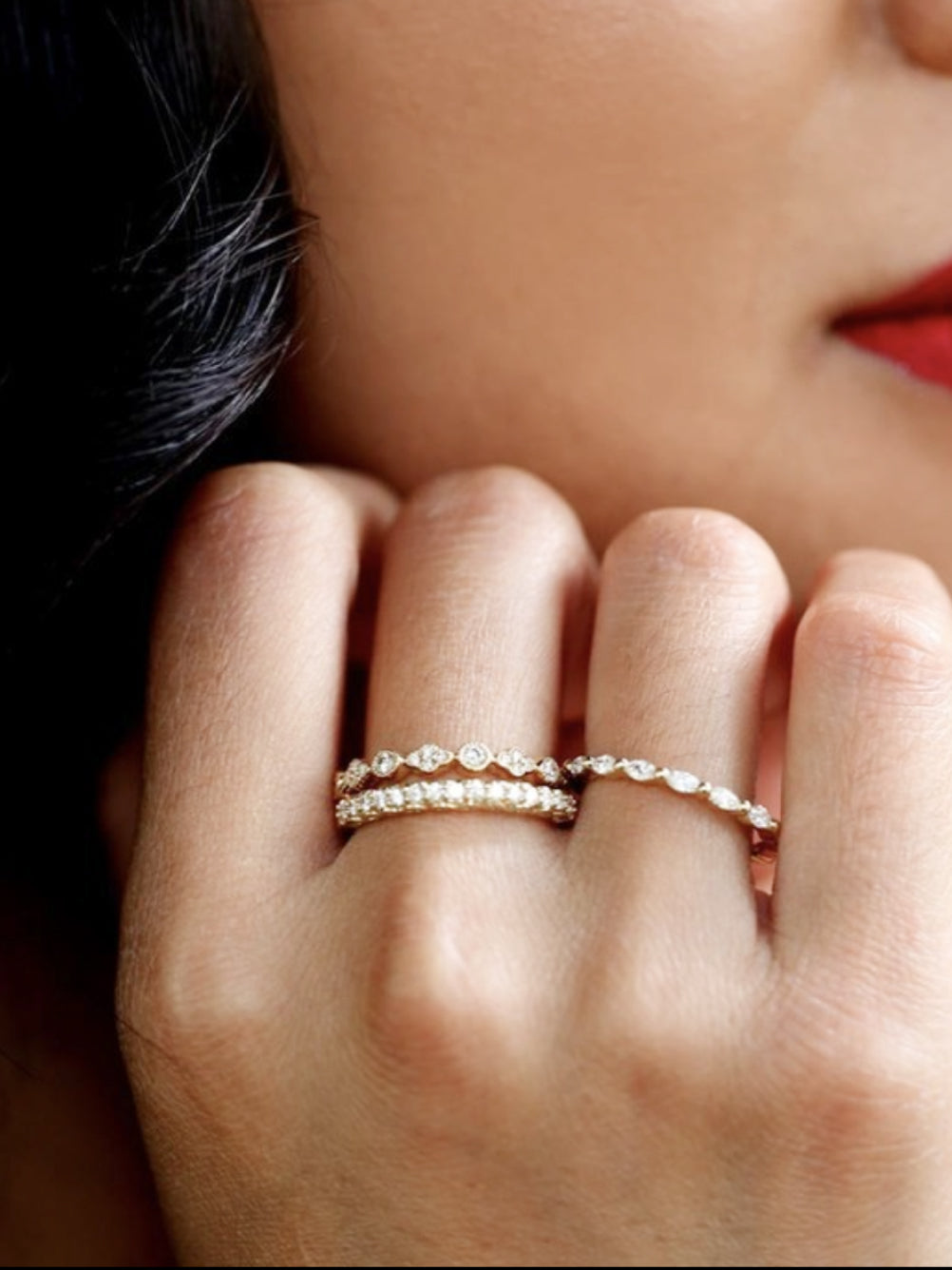 A woman with her left hand up to her cheek flashing our stackable rings on.