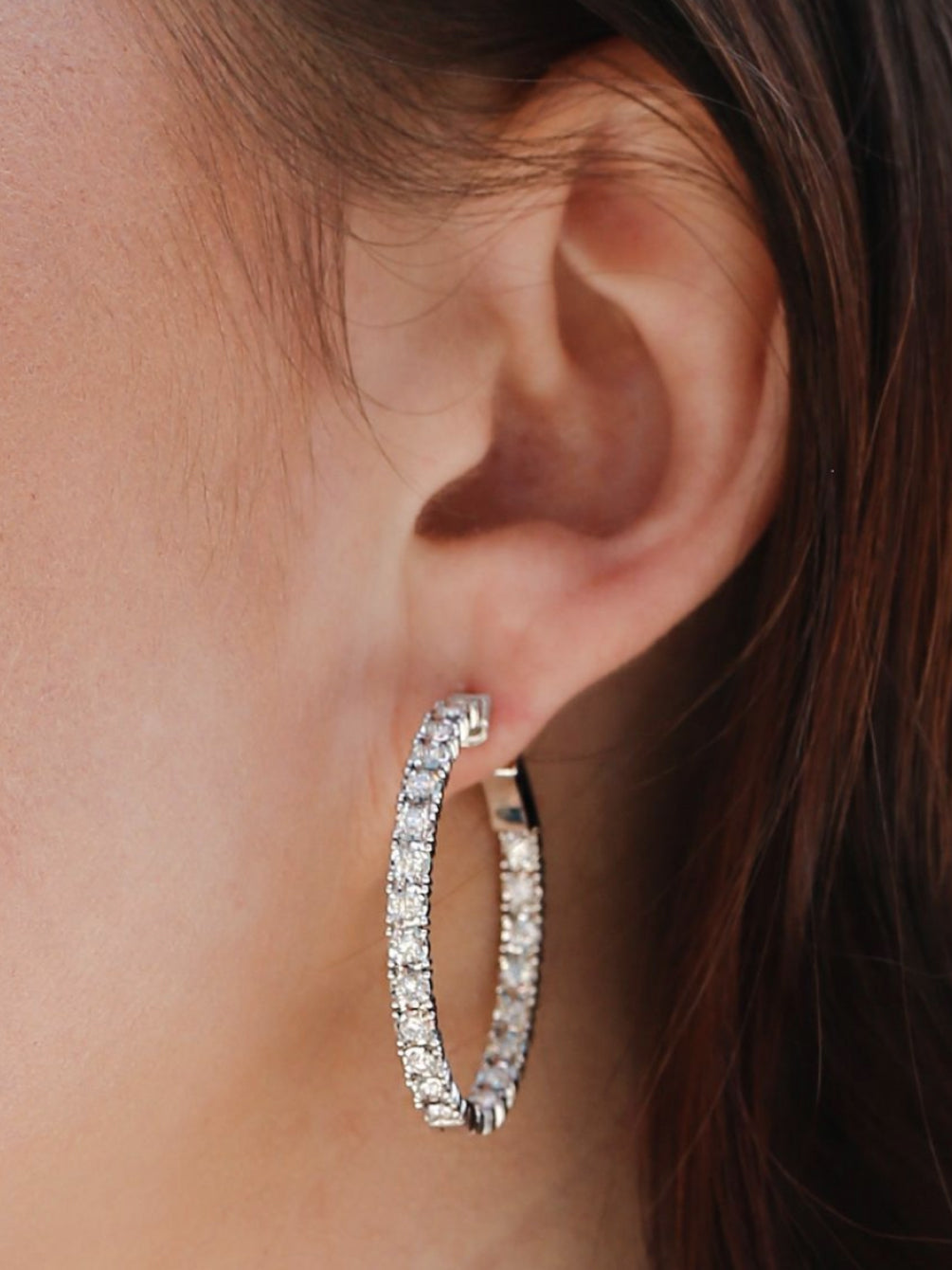 A beautiful diamond white gold hoop earring on a womans left ear lobe