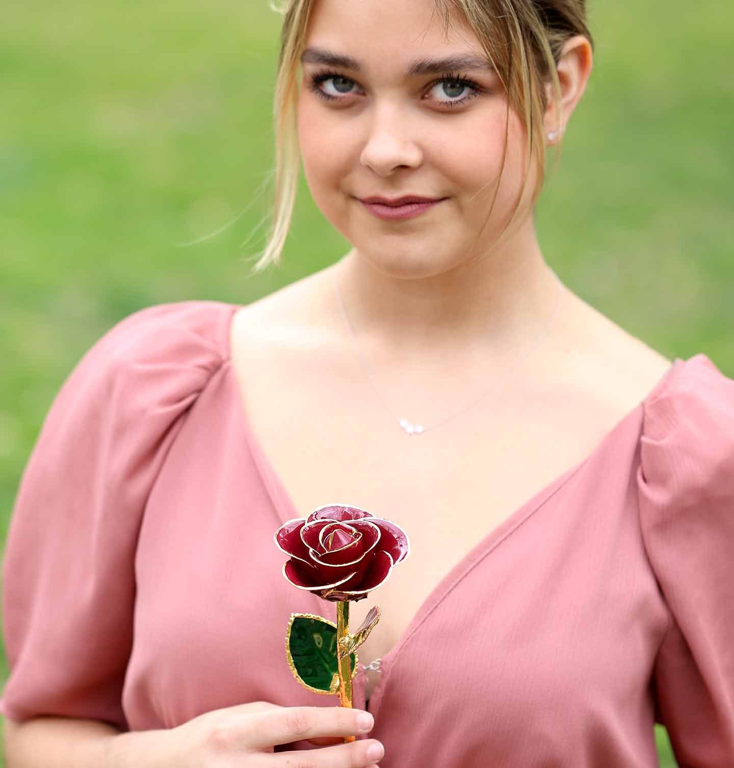 A girl in a mauve shirt with her hair tied back holding our Red Wine 24 Karat Gold Dipped Rose.