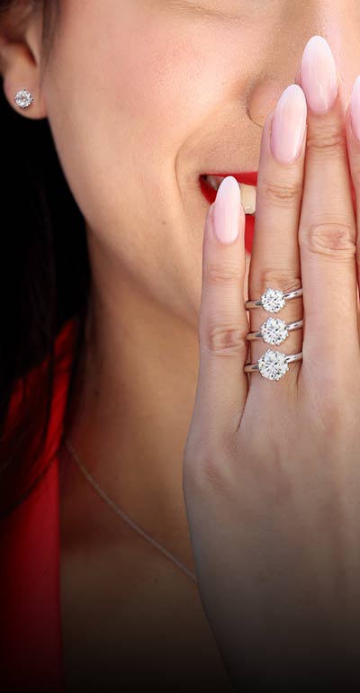A woman covering her smiling face wit 3 different sized but same style rings on her ring finger representing our lifetime full value upgrade option.
