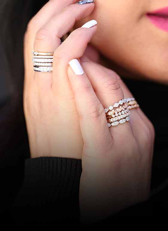 A woman with stacks of rings on both hands featuring different styles and metal colors we offer for women.
