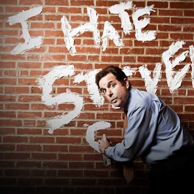 Steve Singer with a spray paint bottle writing "I hate Steven Singer" on to a brick wall.