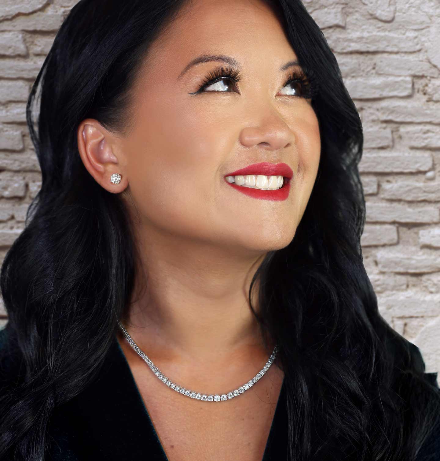 A women wearing a classic diamond tennis necklace and diamond studs with a red lip.