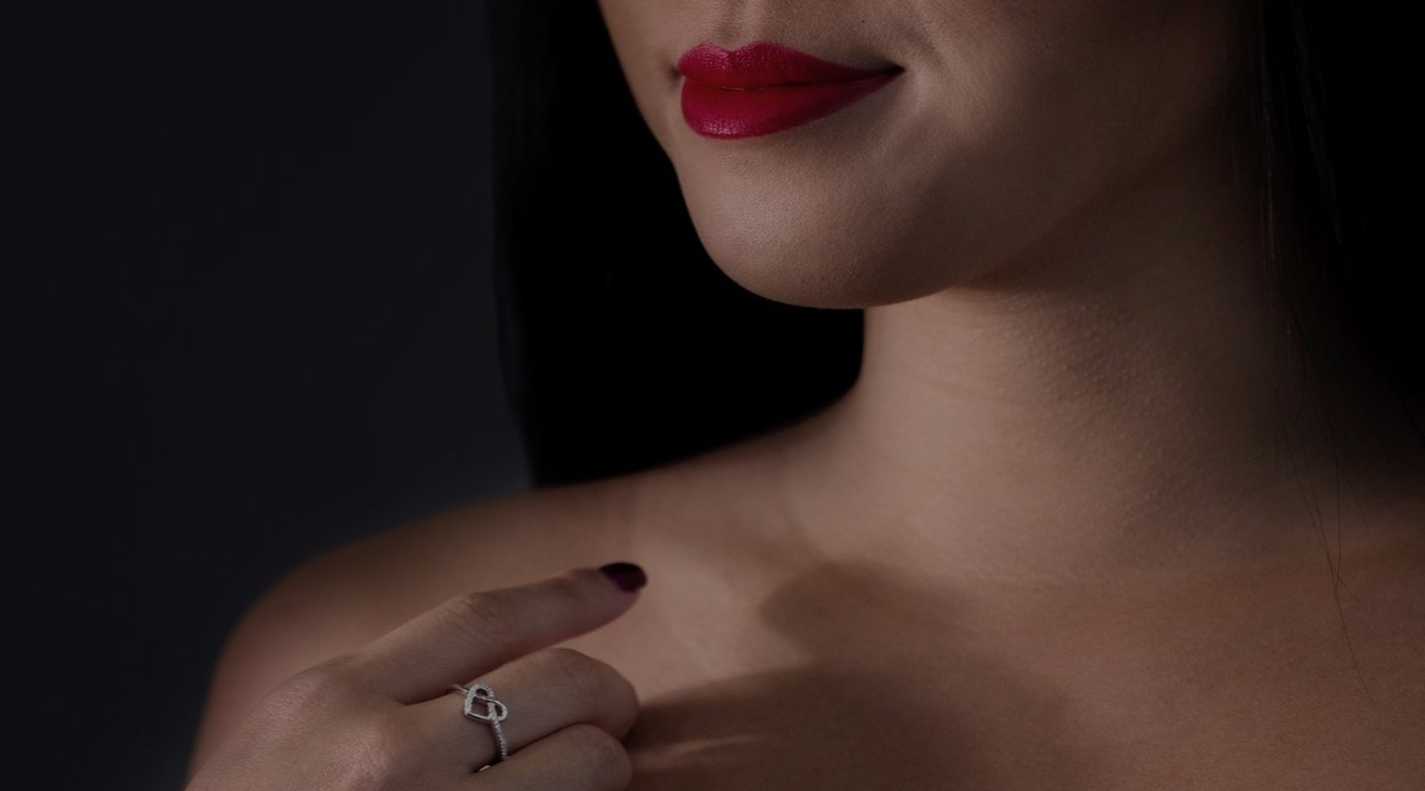 A woman with red lipstick on has her hand on her chest showing off our diamond heart ring from our heart jewelry collection 