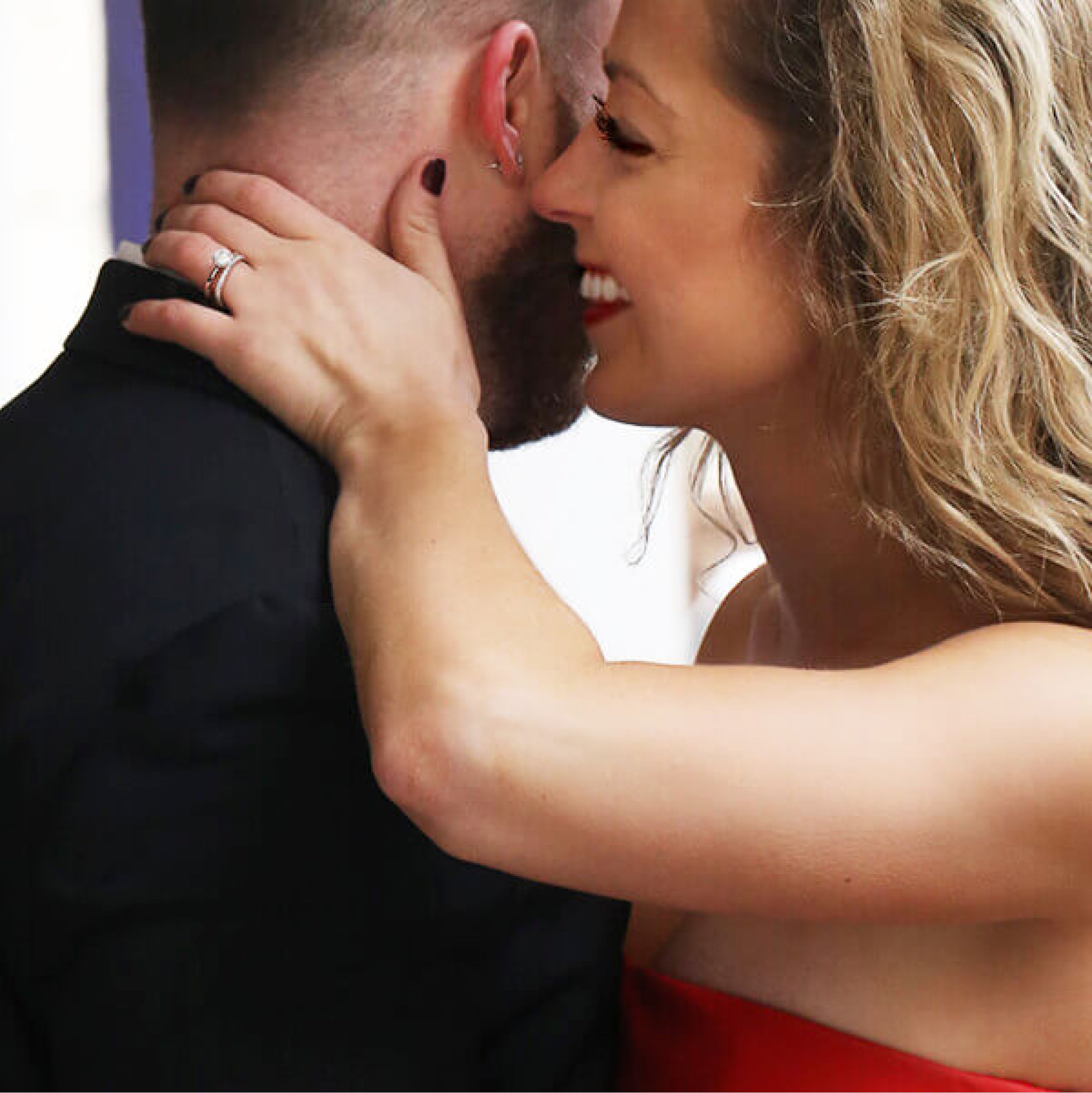 A woman smiling with her hand on her mans neck showing her diamond engagement ring.