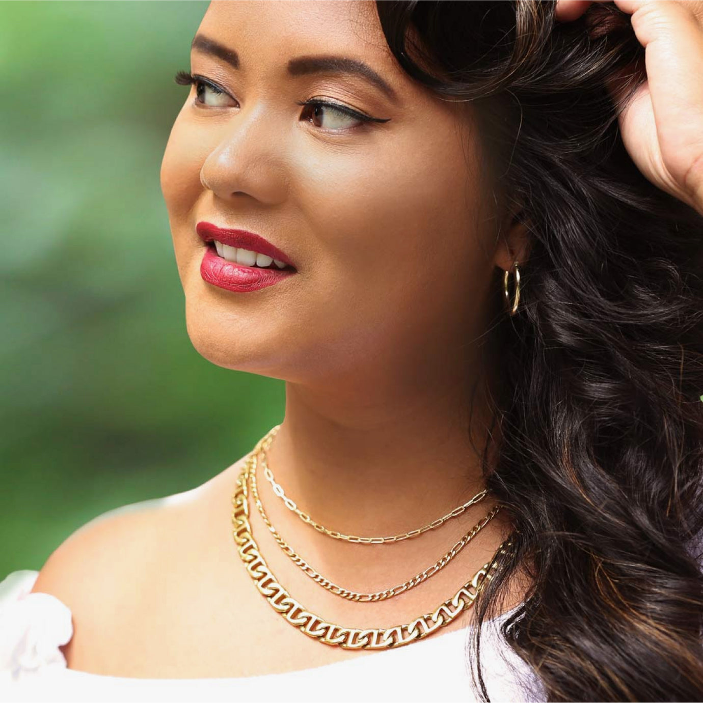 A woman demonstrating how to mix thick and thinner chains together for a layered look.